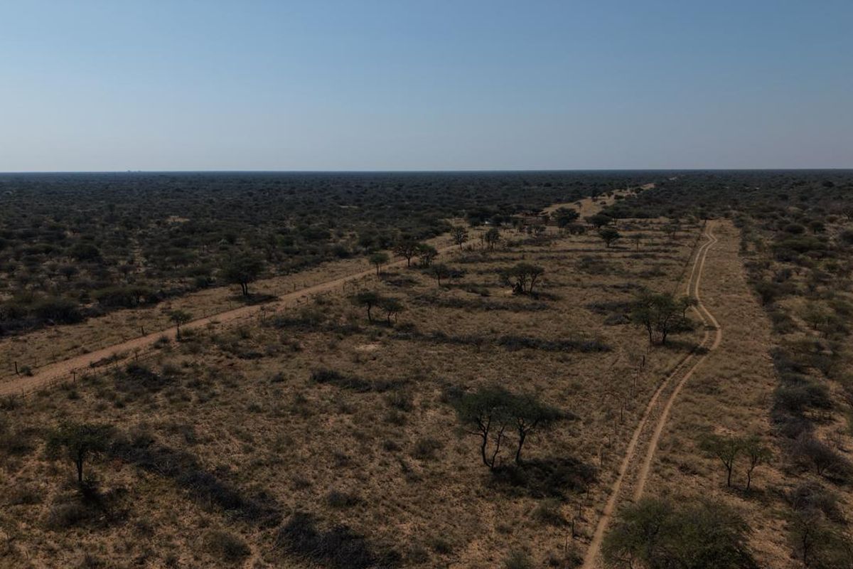 An aerial view of expansive farm land featuring natural vegetation, dirt access tracks, and perimeter fencing.