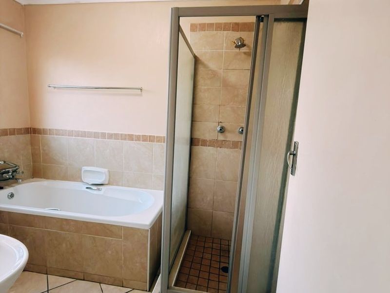 A functional bathroom featuring a built-in bathtub, a separate shower enclosure, and neutral tiled finishes throughout.