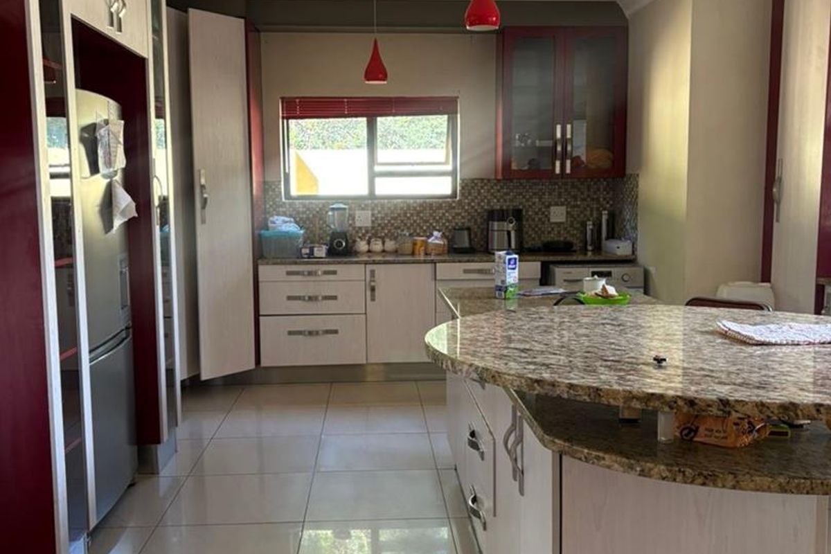 Spacious kitchen featuring granite countertops, a central island with breakfast bar, tiled flooring, and built-in cabinetry with a modern two-tone finish.
