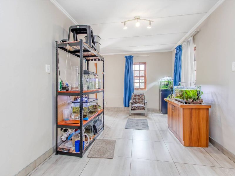 A neutrally painted living area featuring tiled flooring, coved ceilings, and track lighting, offering a versatile space for various interior design layouts.