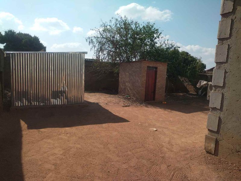 Rear yard area featuring a corrugated metal shed, a small brick outbuilding, and an enclosed perimeter wall with unpaved ground.
