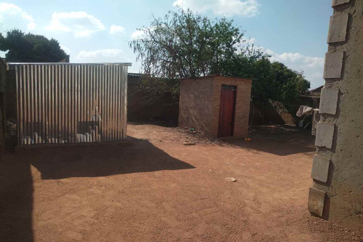 Rear yard area featuring a corrugated metal shed, a small brick outbuilding, and an enclosed perimeter wall with unpaved ground.