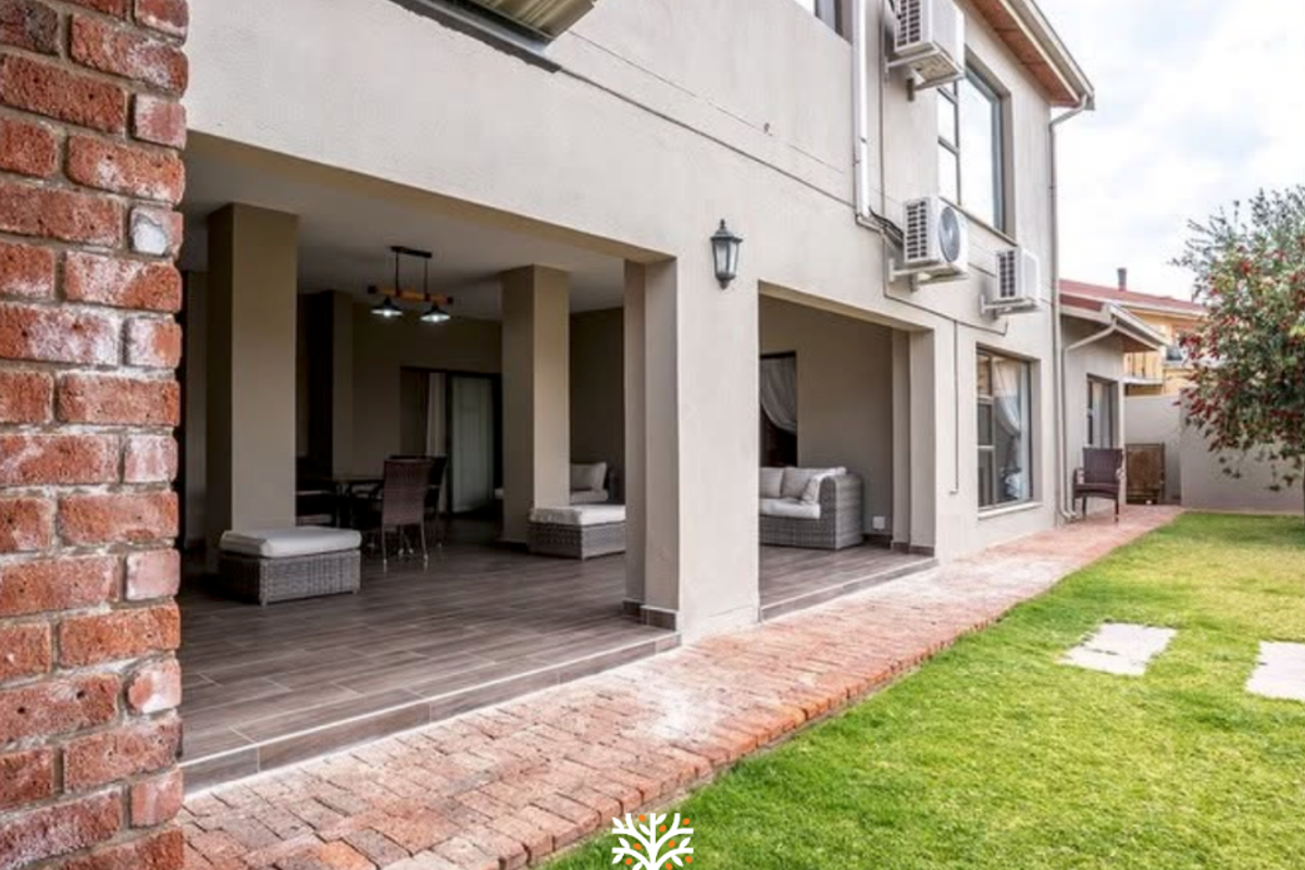 Spacious covered patio featuring tiled flooring and brick accents, overlooking a well-maintained garden area with exterior wall-mounted air conditioning units.