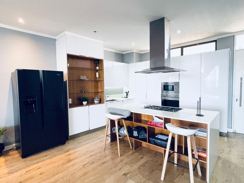 Modern kitchen featuring high-gloss white cabinetry, a central island with a gas hob, integrated appliances, and warm wood-toned shelving and flooring.