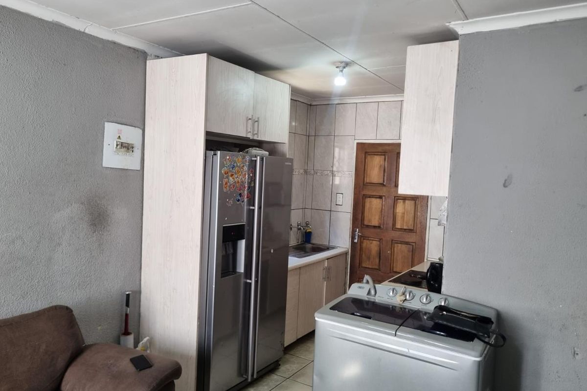 A compact kitchen area featuring built-in cabinetry, tiled backsplash, and tiled flooring, requiring some cosmetic updates to improve the overall finish.