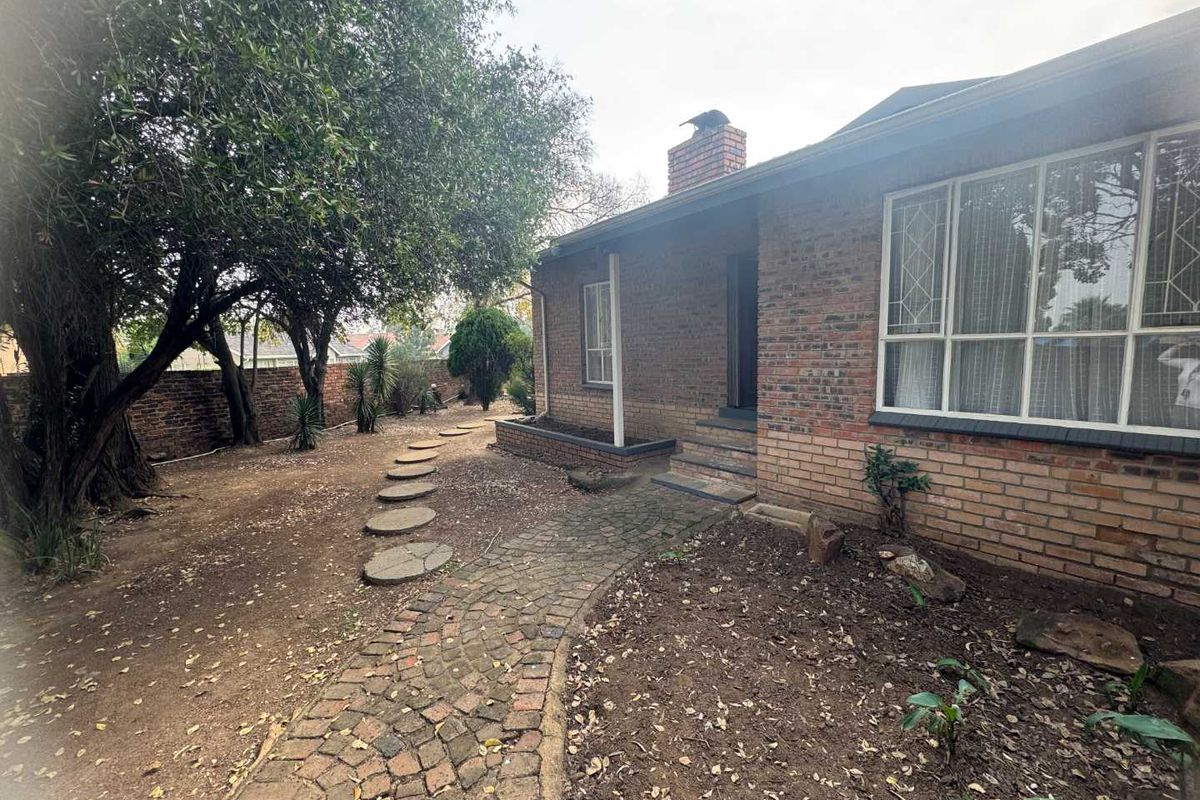 A view of the rear exterior of the house featuring a brick facade, a chimney, and a paved walkway leading through the garden area.