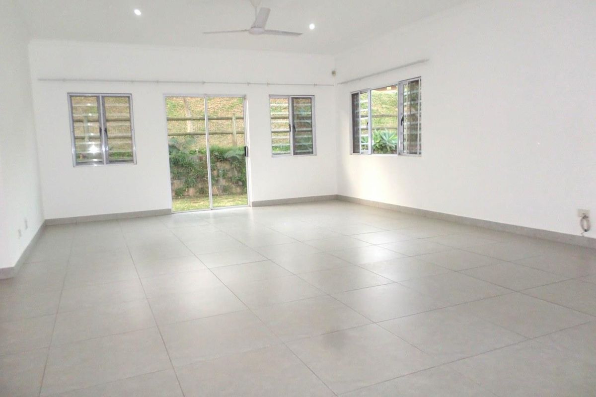 A spacious, bright, and empty living area featuring neutral tiled flooring, recessed lighting, a ceiling fan, and large aluminium windows and sliding doors.