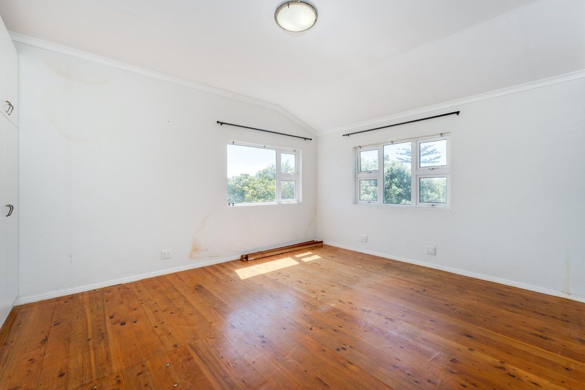 An empty bedroom featuring original timber flooring, built-in cupboards, and dual aspect windows. The walls show visible signs of water staining.