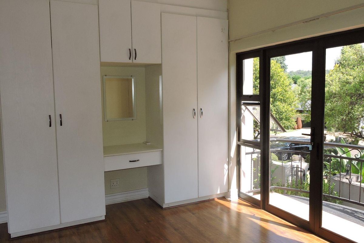 Bright bedroom featuring built-in cupboards with a central vanity, laminate flooring, and a sliding glass door opening onto a private balcony.