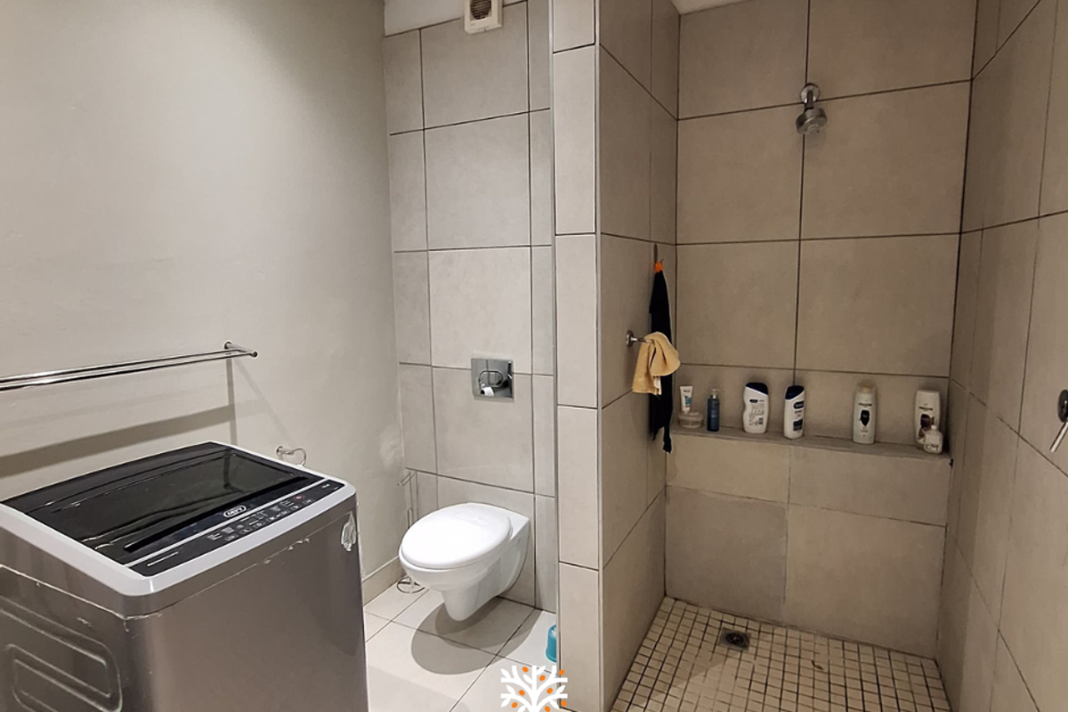 A functional bathroom featuring a walk-in shower with tiled walls, a wall-mounted toilet, and a dedicated space for laundry appliances.
