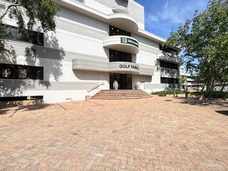 Front elevation of a multi-story commercial office building featuring a paved entrance area, brick stairs, and modern architectural facade.