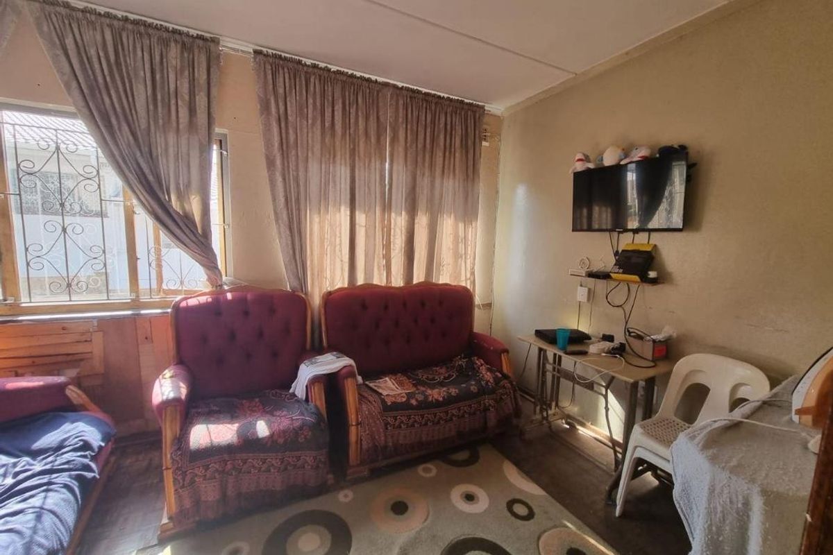 A living room area featuring security bars on the windows and dated wall finishes, offering potential for cosmetic updates and modernization.