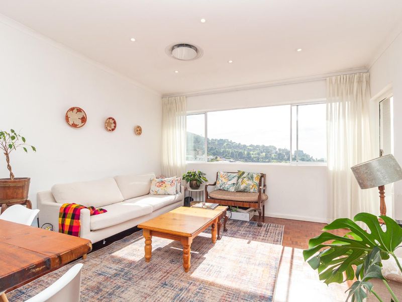 A bright and airy living room featuring classic parquet flooring, recessed lighting, and a large window offering scenic views.