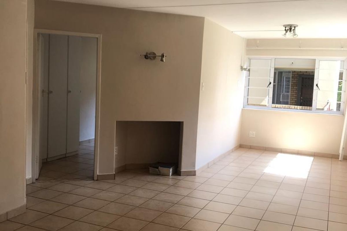 An empty, open-plan living area featuring tiled flooring, a built-in fireplace, and neutral walls, offering a blank canvas for interior design.