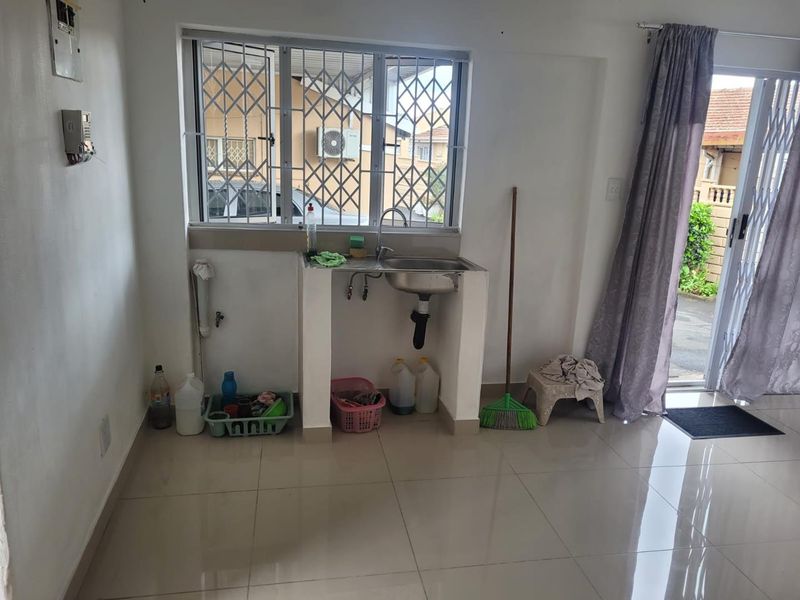 A functional scullery or utility area featuring a stainless steel sink, tiled flooring, and direct access to an outdoor patio area.