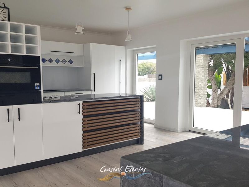 Modern kitchen featuring sleek white cabinetry, dark stone countertops, a central island, and direct access to the outdoor patio area.