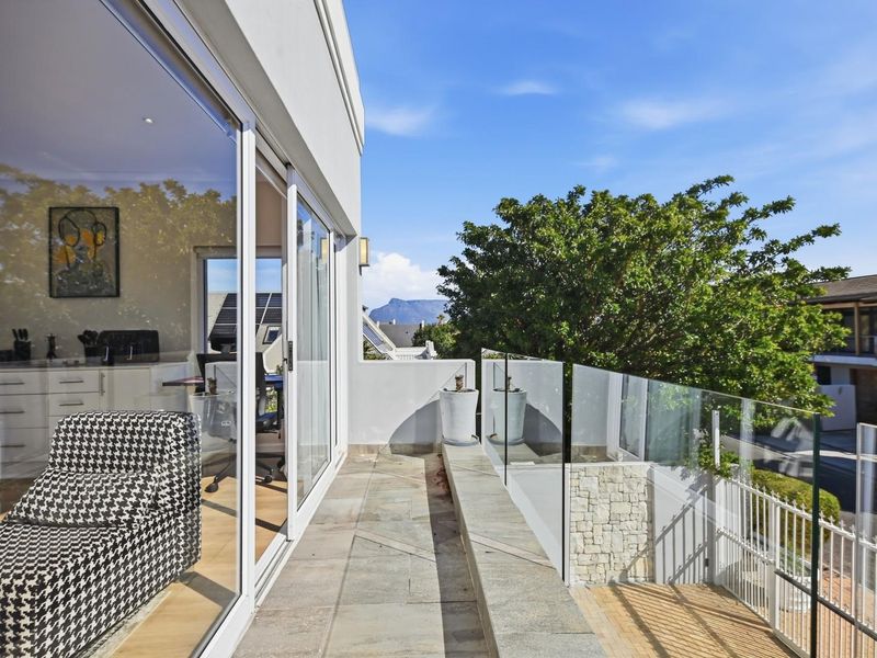 A modern balcony featuring a sleek glass balustrade, stone tile flooring, and direct access to the interior through large sliding glass doors.