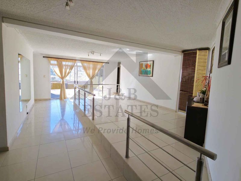 Spacious living area featuring tiled flooring, a modern stainless steel balustrade, and large sliding glass doors leading to an outdoor space.