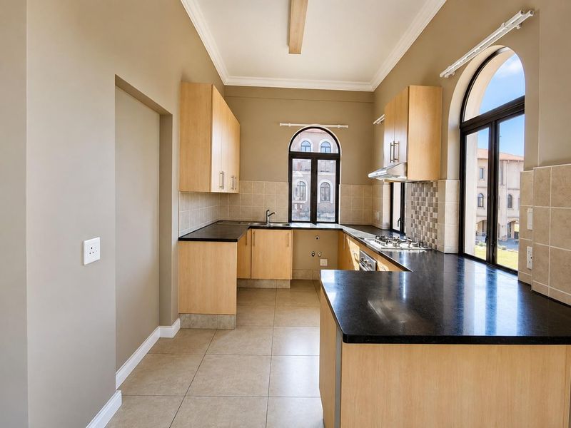 A clean, functional kitchen featuring light wood cabinetry, dark granite countertops, a gas hob, and arched windows providing natural light.