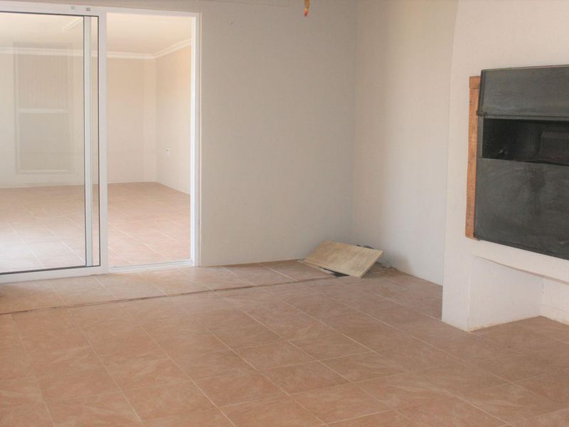 An empty covered patio area featuring tiled flooring, a built-in fireplace, and sliding glass doors leading to an adjacent interior room.