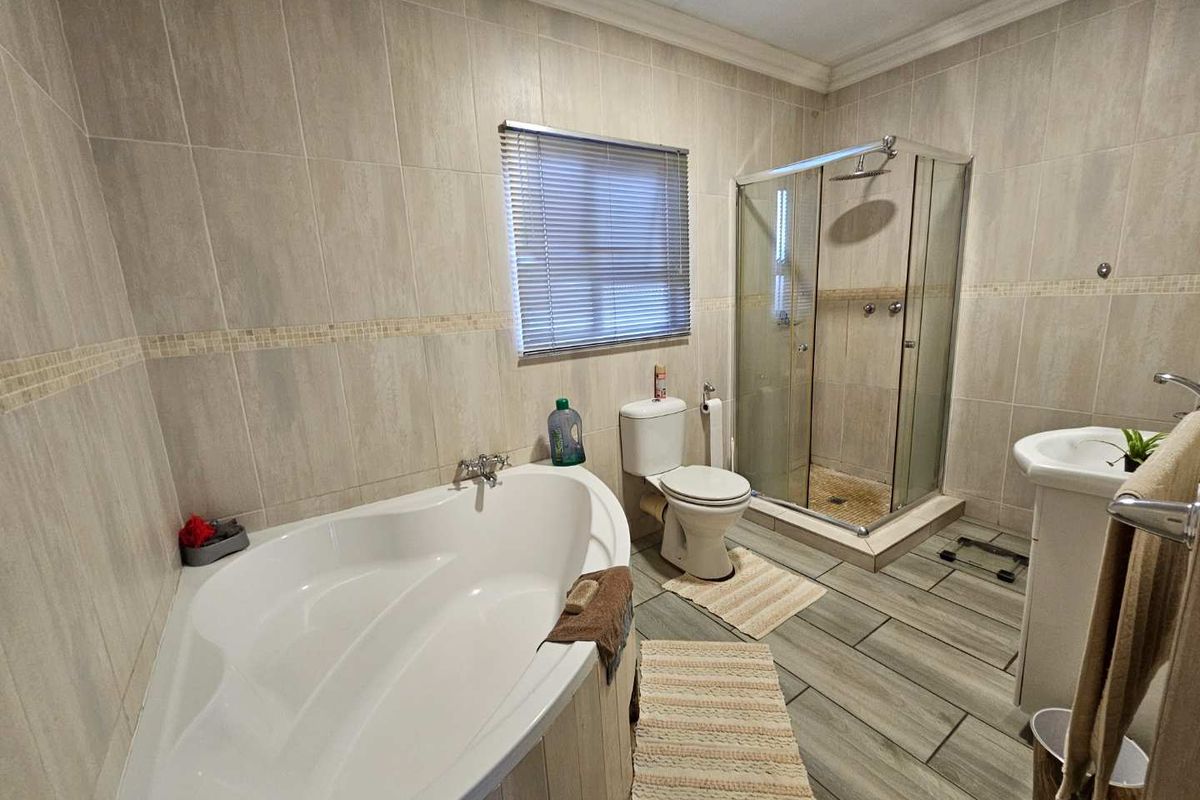 A well-maintained bathroom featuring a corner bathtub, a separate glass-enclosed shower, a toilet, and a pedestal basin with neutral wall and floor tiling.