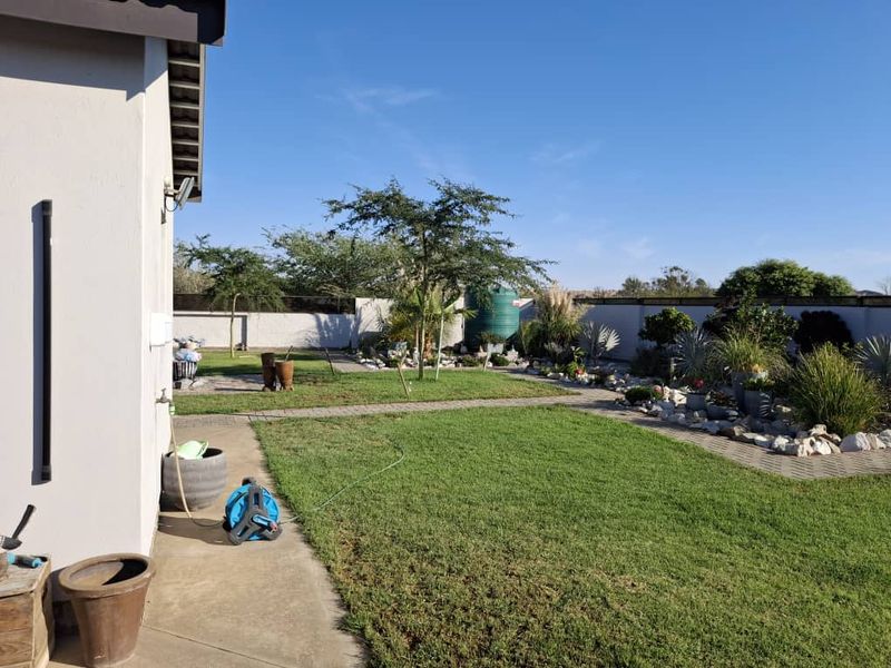 A well-maintained rear garden featuring a manicured lawn, paved pathways, boundary walls, and a water tank, providing a neat and functional outdoor space.