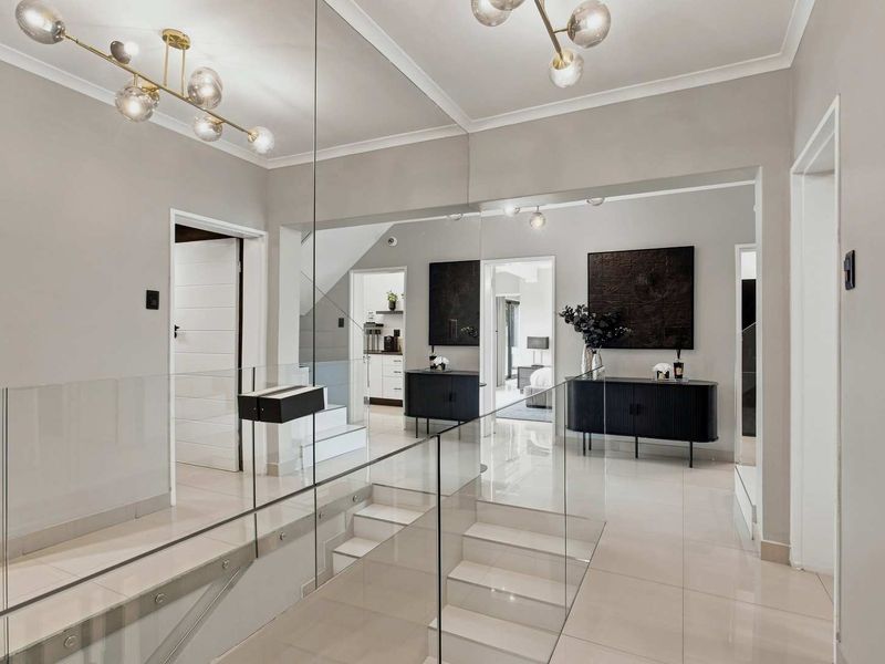 Modern hallway featuring a glass balustrade, polished tiled flooring, and a large mirrored wall, creating a bright and spacious transition area.