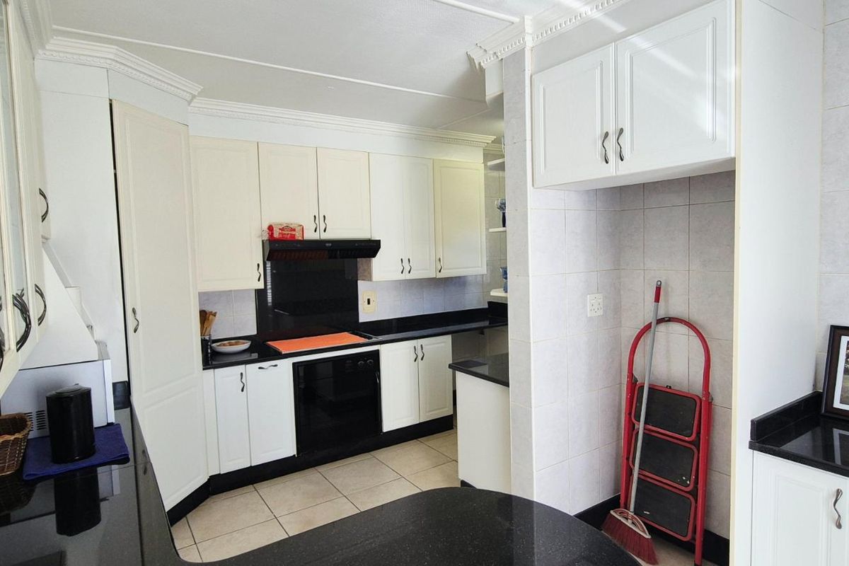 A functional kitchen featuring white cabinetry, black granite countertops, integrated oven, extractor fan, and tiled finishes throughout.