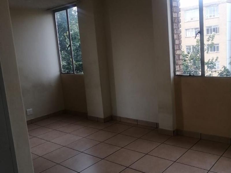 An empty living area featuring tiled flooring and large windows, providing ample natural light. The space requires minor cosmetic updates to the walls and ceiling.