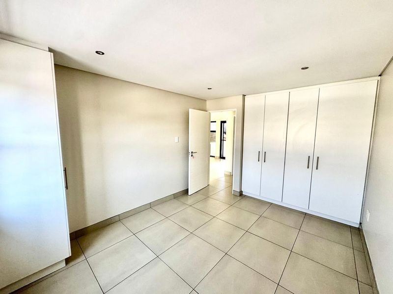 A bright, empty bedroom featuring neutral tiled flooring, recessed downlighting, and ample built-in cupboard storage space.