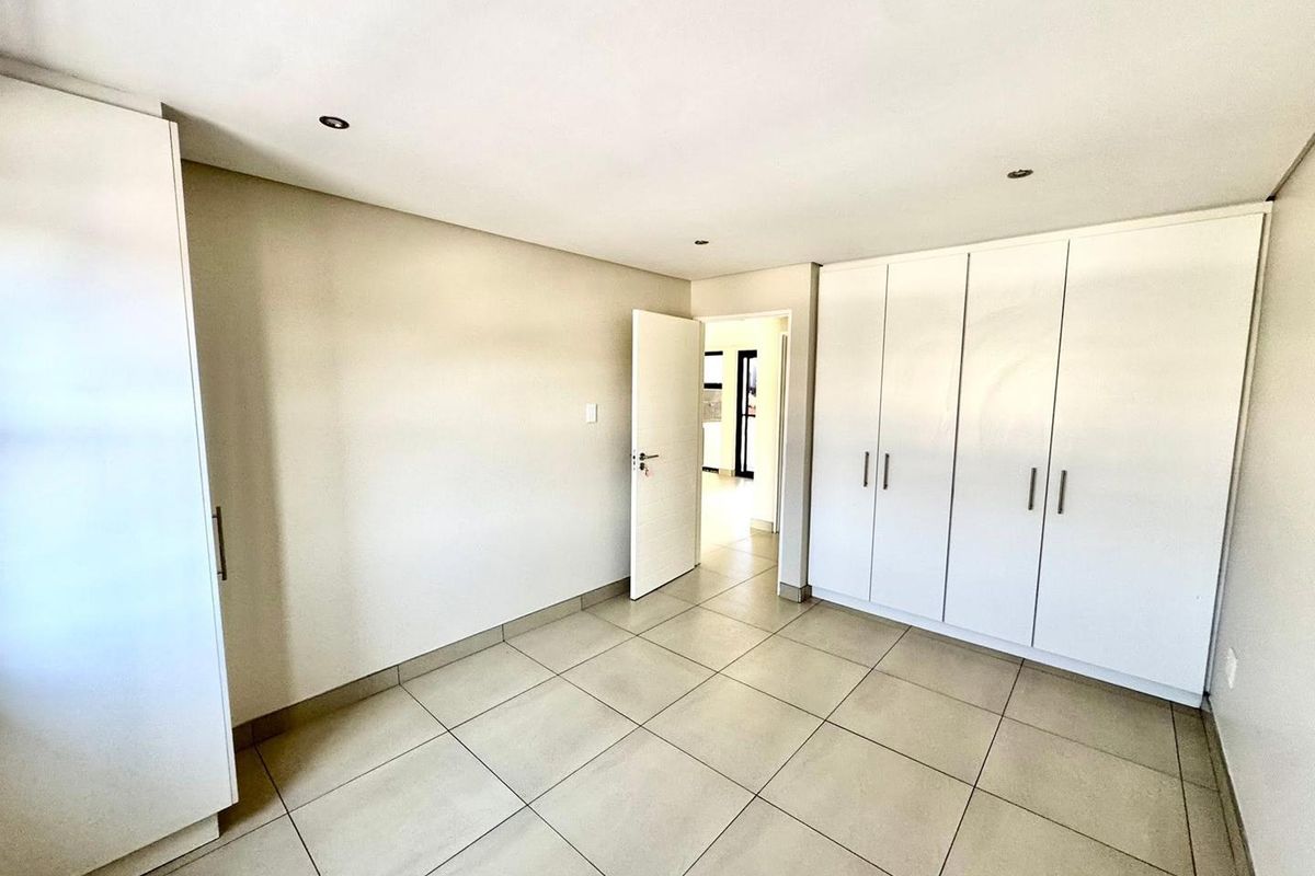 A bright, empty bedroom featuring neutral tiled flooring, recessed downlighting, and ample built-in cupboard storage space.