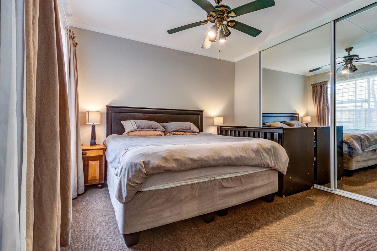 A well-maintained bedroom featuring a ceiling fan and large mirrored sliding wardrobe doors, providing ample storage and reflecting natural light.