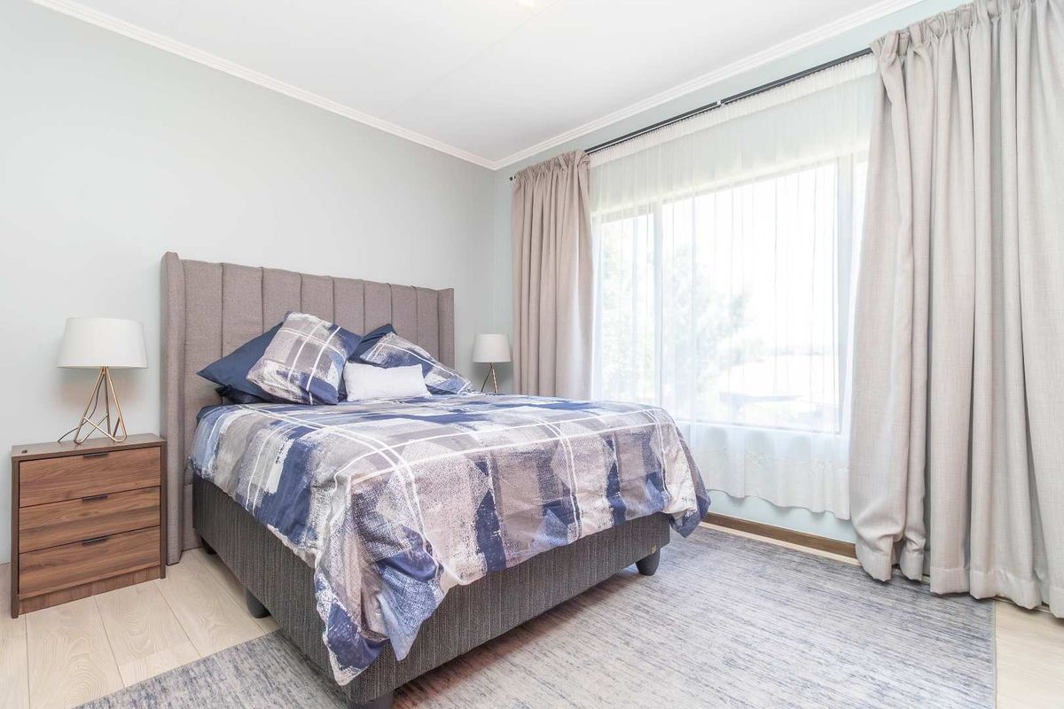 A well-maintained bedroom featuring light-toned laminate flooring, crown molding, and a large window with integrated curtain tracks.