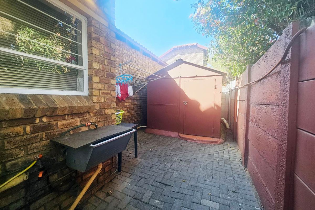 A paved rear courtyard area featuring a brick boundary wall, an external utility sink, and a standalone storage shed.