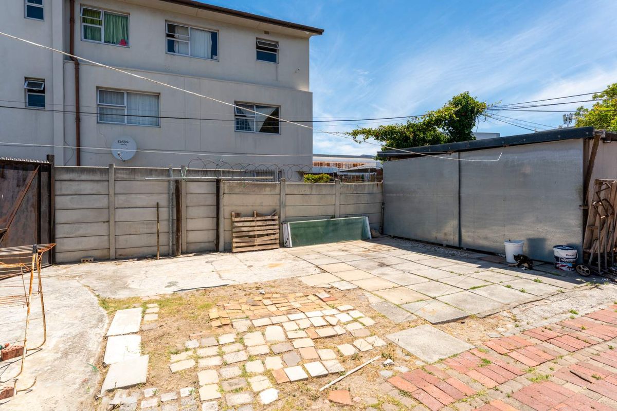 A rear outdoor area featuring a mix of concrete and brick paving, enclosed by a precast concrete wall and a metal storage structure.