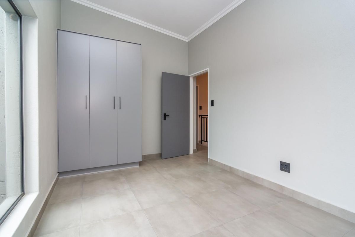 A bright, modern bedroom featuring neutral tiled flooring, built-in grey cabinetry, and clean finishes, offering a versatile space ready for personalization.