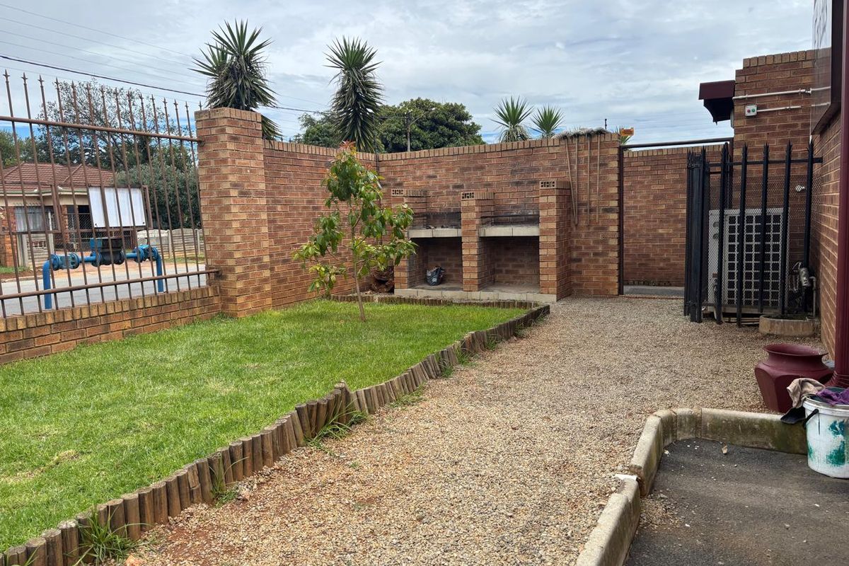 A private outdoor area featuring a built-in brick braai, a small lawn, and gravel pathways enclosed by a secure perimeter wall and metal fencing.