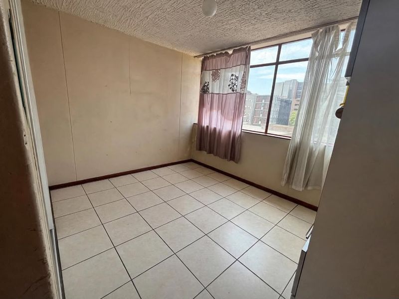 An empty bedroom featuring tiled flooring, large windows providing natural light, and neutral wall finishes, ready for personalization.