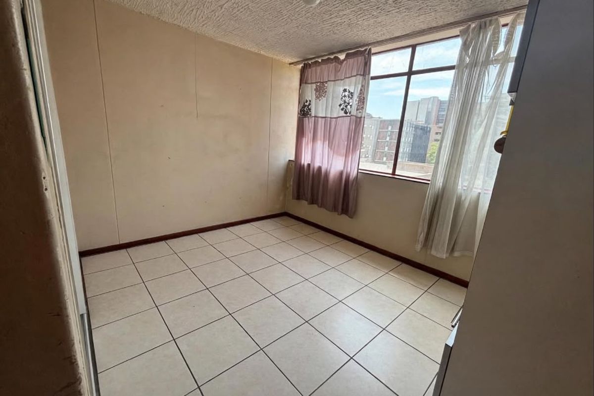 An empty bedroom featuring tiled flooring, large windows providing natural light, and neutral wall finishes, ready for personalization.
