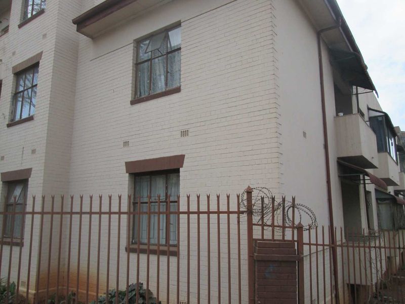 Exterior view of a multi-story apartment building featuring painted brick walls, steel security fencing with razor wire, and integrated balconies.