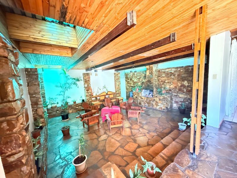 Spacious living area featuring rustic flagstone flooring, exposed timber ceiling beams, a large stone fireplace, and a skylight providing natural light.