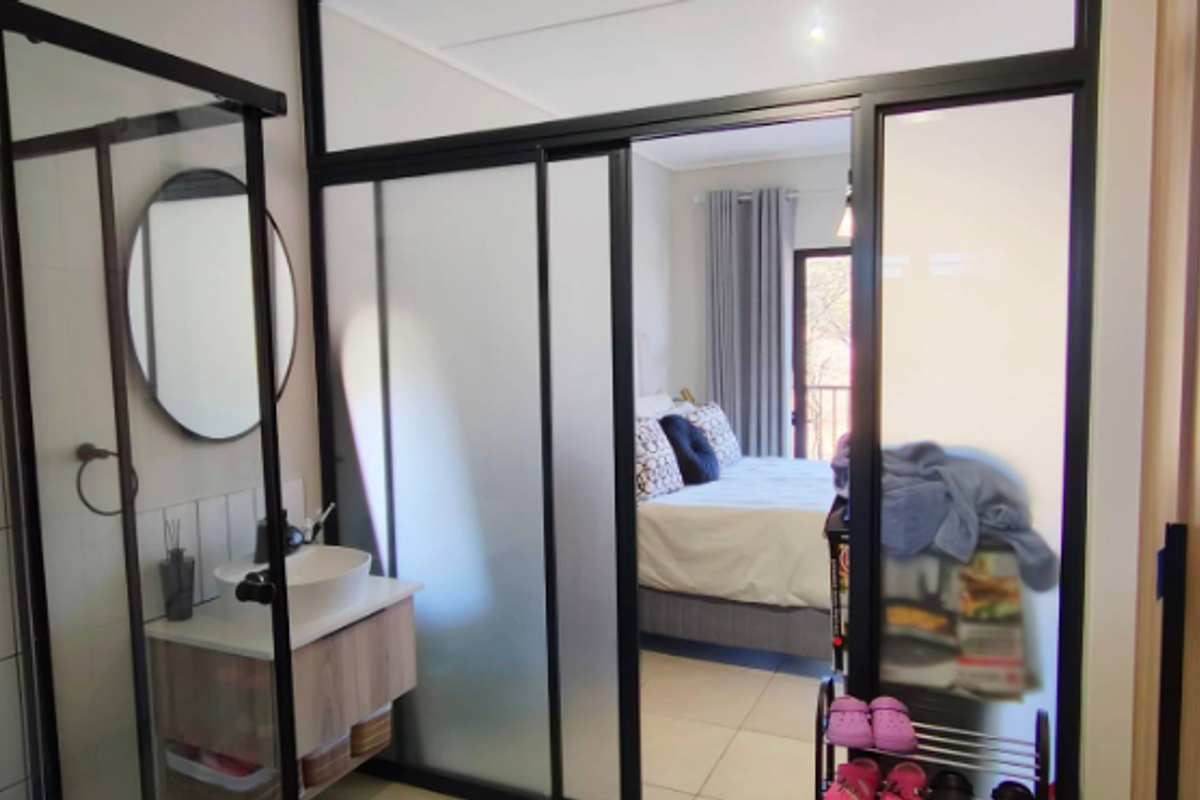 Modern bathroom featuring a glass-enclosed shower, vessel sink with vanity, and a stylish black-framed glass partition separating the space from the bedroom.