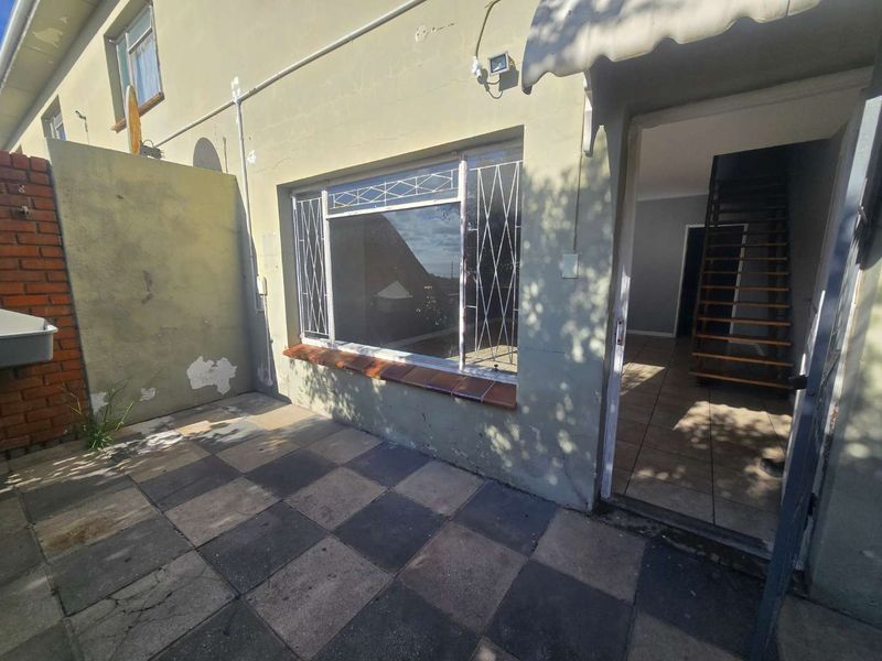 Rear exterior view of the townhouse featuring a paved patio area, security bars on windows, and an external wash basin.