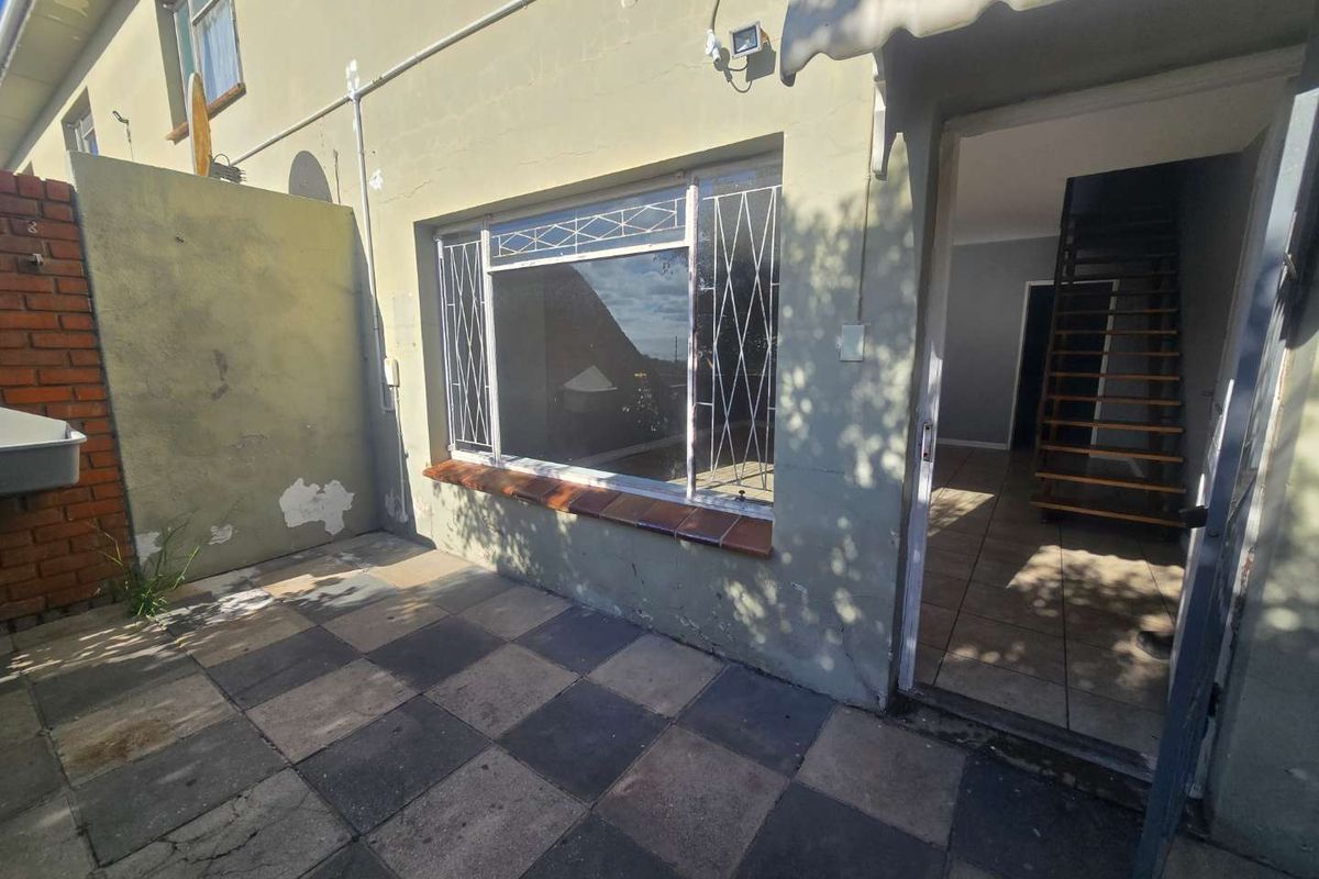 Rear exterior view of the townhouse featuring a paved patio area, security bars on windows, and an external wash basin.