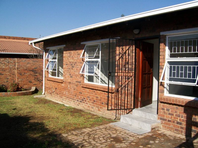 Rear view of a face-brick cluster home featuring a paved patio, security gate, and top-hung windows overlooking a private garden area.