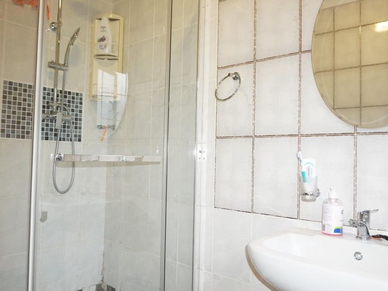 A functional bathroom featuring a glass shower enclosure, wall-mounted basin with mixer tap, and tiled wall finishes.