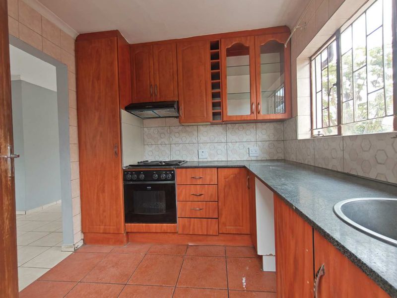 A functional kitchen featuring wooden cabinetry, granite countertops, built-in oven, hob, extractor fan, and tiled finishes throughout.
