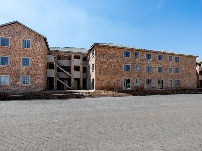 Exterior view of a multi-story face brick apartment complex featuring a large paved parking area and external stairwell access.