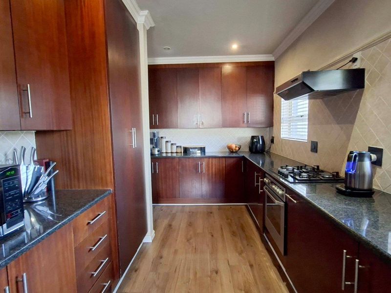A well-maintained kitchen featuring dark wood cabinetry, granite countertops, a gas hob, built-in oven, and a tiled backsplash with laminate flooring.