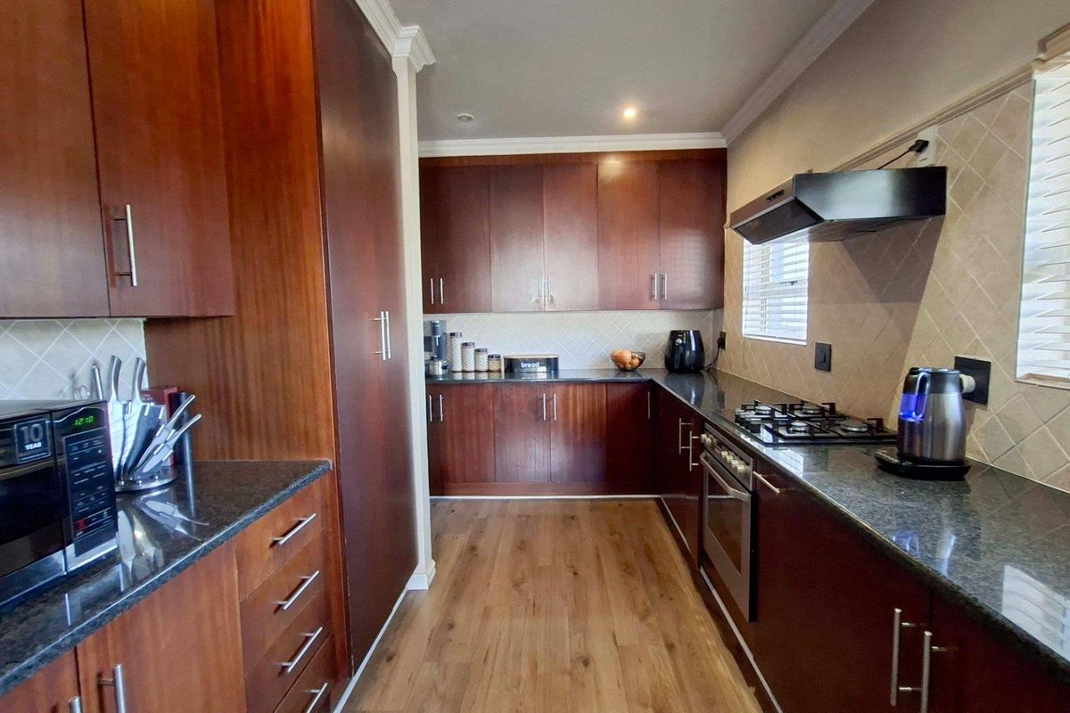 A well-maintained kitchen featuring dark wood cabinetry, granite countertops, a gas hob, built-in oven, and a tiled backsplash with laminate flooring.